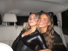 two women in cat costumes sitting in the back seat of a car with their faces painted to look like cats