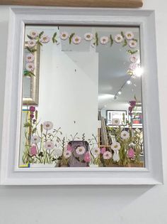 a mirror with flowers painted on it in front of a white wall and wooden frame