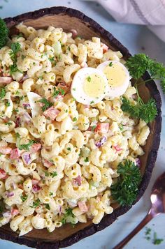 a bowl full of macaroni salad with an egg on top and parsley