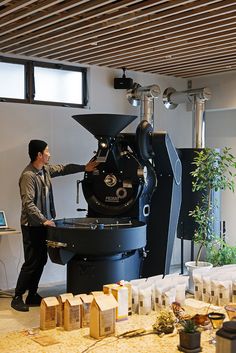 a man standing next to a large machine in a room filled with boxes and plants