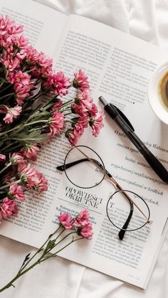 a cup of coffee and some pink flowers on top of an open book next to a pair of glasses