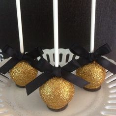 some cake pops are on a white plate with black ribbon and gold glittered balls