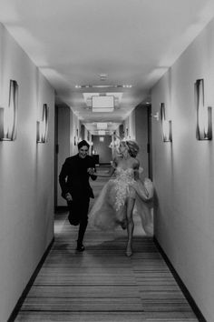 a man and woman walking down a long hallway with lights on either side of them