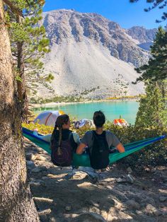 two people sitting in a hammock looking out over a mountain lake and mountains