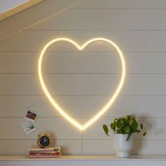 a heart - shaped neon sign on the wall above a mantle with a potted plant