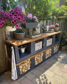 a wooden table with flowers and other items on it in a garden area next to a fence