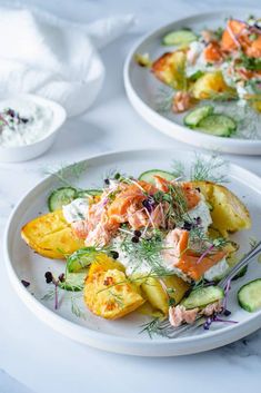 two white plates topped with food on top of a marble countertop next to cucumbers