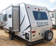 an rv is parked on the gravel in front of another trailer that has its door open