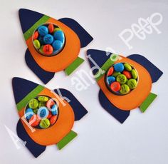 three felt toy rockets with buttons in them on a white surface, one is blue and the other is orange