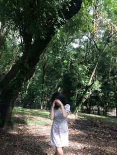 a woman standing in the middle of a forest with her hands on her head and looking up