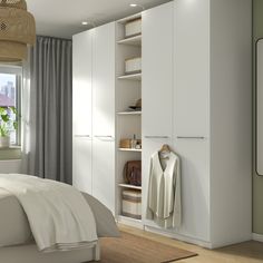 a bedroom with white cupboards and clothes hanging on the wall next to a bed