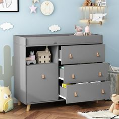 a baby's room with blue walls and wooden flooring, including a grey dresser