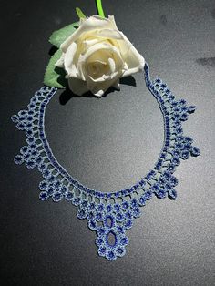 a white rose sitting on top of a table next to a blue and white necklace