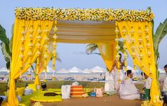 an outdoor ceremony with yellow drapes and white flowers on the altar, surrounded by palm trees