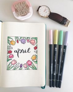 an open notebook with the word april surrounded by markers and pens