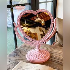 a pink heart shaped mirror sitting on top of a wooden table