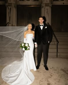 a bride and groom standing in front of stairs