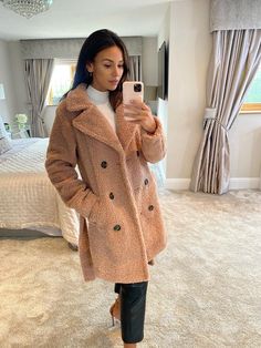 a woman taking a selfie while wearing a coat and leggings in a bedroom