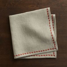 two linen napkins with red stitching on them sitting on top of a wooden table