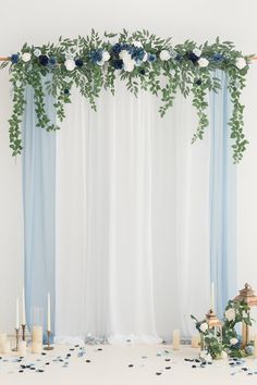 the wedding arch is decorated with blue and white flowers, greenery, and candles