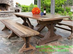 a wooden picnic table with two benches and a bottle of wine on the table in front of an outdoor fireplace