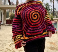 a woman standing in front of a pool wearing a colorful sweater