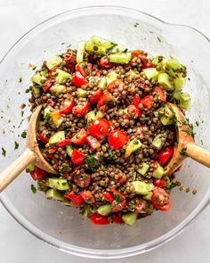 a glass bowl filled with lentils, tomatoes and cucumbers