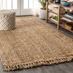 a large rug with fringes on the floor in front of a wooden table and bookshelf