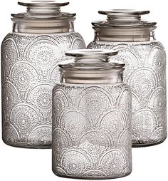 three glass jars with metal lids on each one and an ornate design in the middle