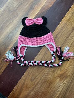 a crocheted minnie mouse hat on top of a wooden floor with pink and black trim