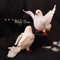 two knitted white doves sitting next to each other on top of a black surface