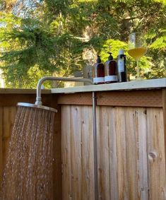 a shower head with water running from it next to a wooden fence and pine trees in the background