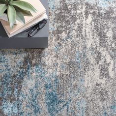 an area rug with a book, glasses and plant on it next to a pair of eyeglasses