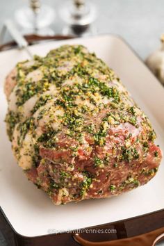 a piece of meat covered in herbs and seasoning on a white plate next to garlic