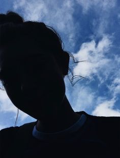 the silhouette of a woman's head against a blue sky with clouds in the background