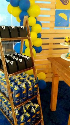 a ladder is next to a table with blue and yellow decorations on it, while balloons are in the background