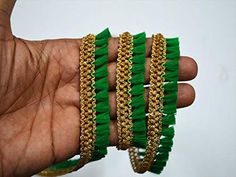 a hand is holding some green and gold bracelets