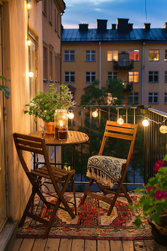 A small apartment balcony with a cozy seating nook featuring a round table and two chairs, adorned with potted plants and string lights. The balcony offers a picturesque view of a tree-lined street and neighboring buildings at sunset, creating a warm and inviting atmosphere. Small Outside Balcony Ideas, Flat With Balcony, Apartment Small Balcony Ideas, Tiny Apartment Balcony Ideas, Airbnb Balcony Ideas, Balcony Ideas Small Spaces, Uncovered Balcony Ideas, Small House Ideas Decorating, Small Balcony Aesthetic