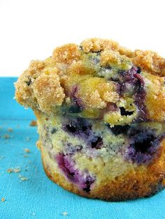 a blueberry muffin with crumbs on top sitting on a blue cloth