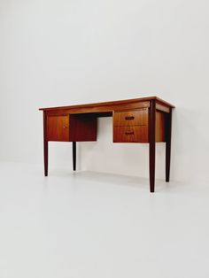 a wooden desk with two drawers sitting on top of white flooring next to a wall