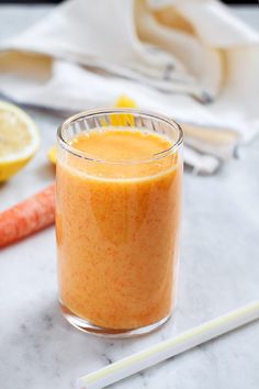 a glass filled with orange juice next to carrots and lemon