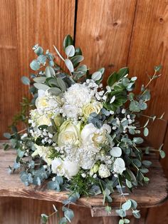 a bouquet of white flowers and greenery on a wooden table in front of a wood paneled wall