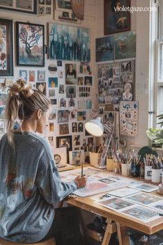 a woman sitting at a desk in front of a window with lots of pictures on the wall