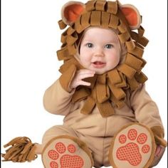 a baby in a lion costume sitting on the ground with its paws up to his face