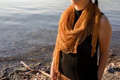 a woman standing by the water wearing a brown scarf and black shirt with braids on her head