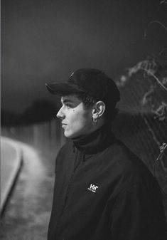 a man standing next to a fence with ear buds in his ears and wearing a hat