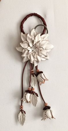 a white flower is hanging from a brown leather cord with leaves and flowers on it