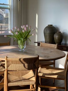 a vase with flowers on top of a wooden table next to two chairs and a window