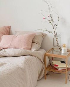 a bed with pink pillows and blankets in a white room next to a small table