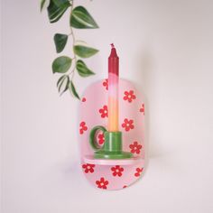 a green cup with a candle in it sitting on a pink shelf next to a potted plant